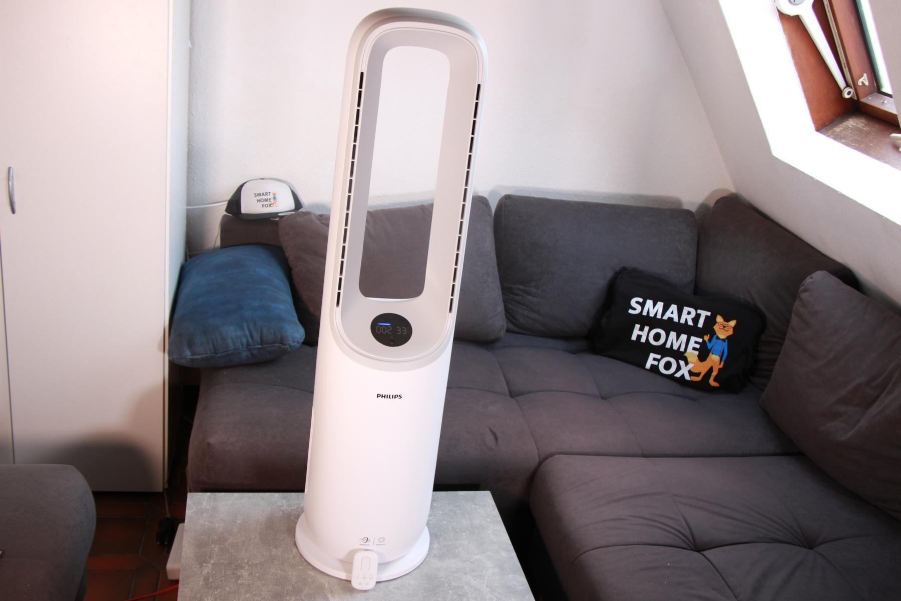 Philips Air Performer Series 7000 стоит во всем своем великолепии на журнальном столике перед диваном, а пульт дистанционного управления прислонен к подставке. 